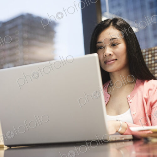 View of an Asian businesswoman working on a laptop computer in her office with a view… View of an Asian businesswoman working on a laptop computer in her office with a view…