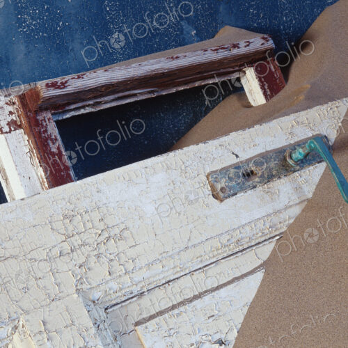 View of battered wooden door buried in sand. View of battered wooden door buried in sand.