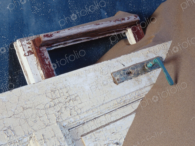 View of battered wooden door buried in sand.