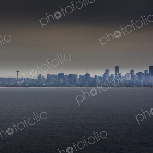 View of the cityscape of Seattle from the water in low light, under a moody sky. View of the cityscape of Seattle from the water in low light, under a moody sky.