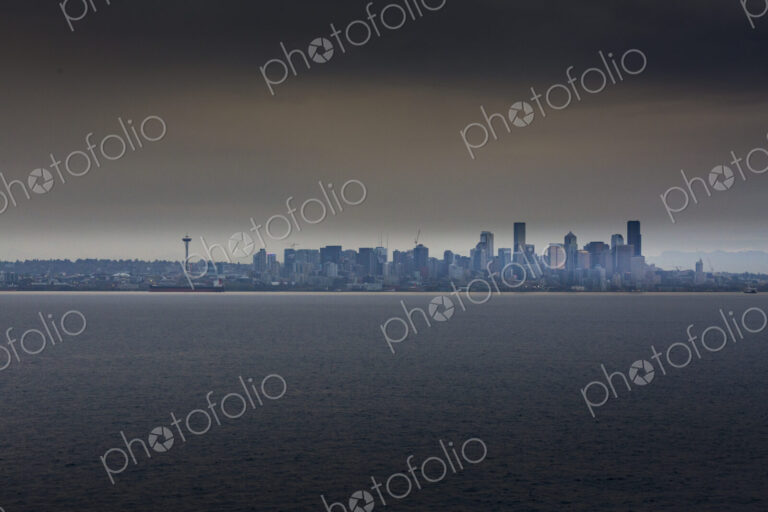 View of the cityscape of Seattle from the water in low light, under a moody sky.