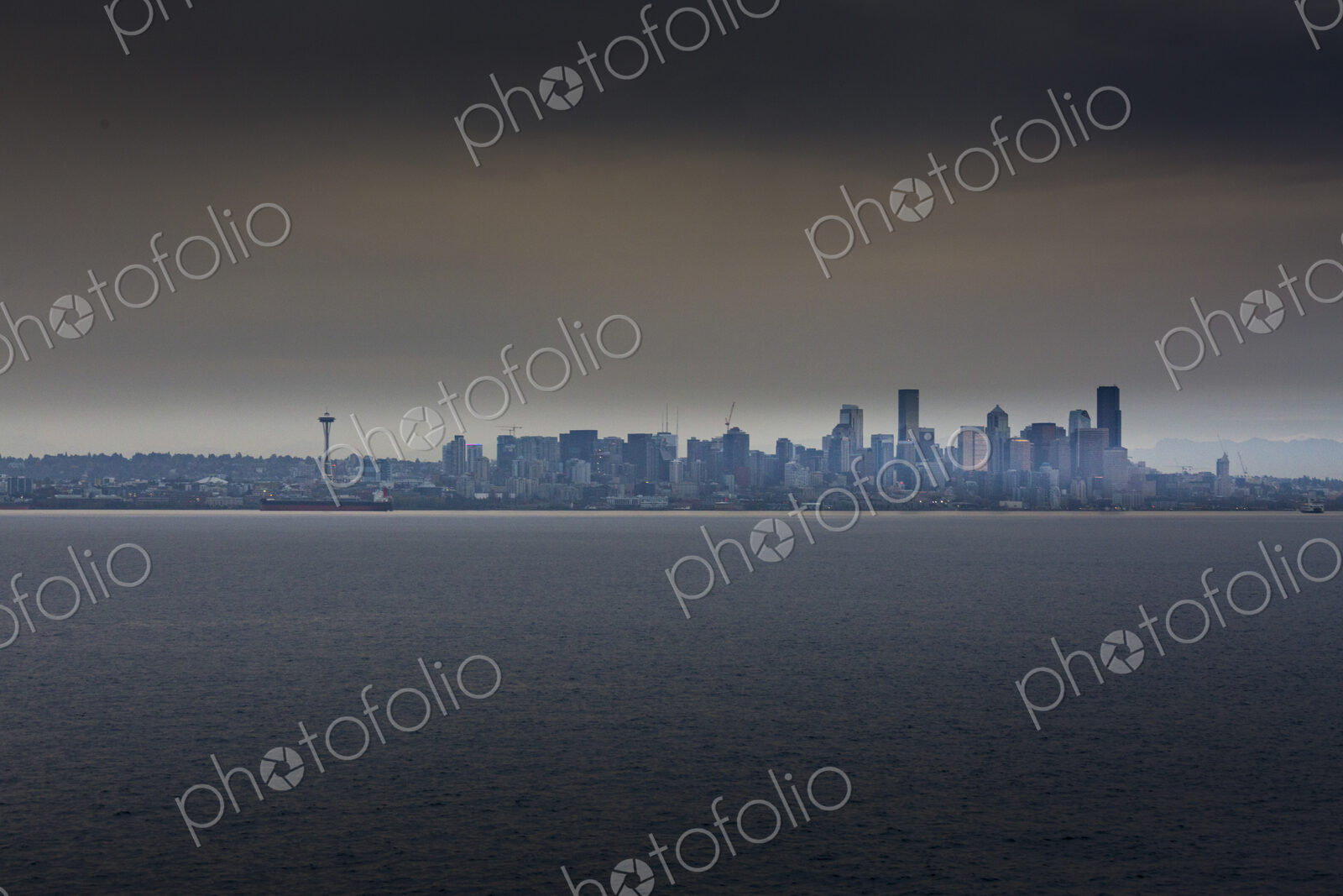 View of the cityscape of Seattle from the water in low light, under a moody sky.