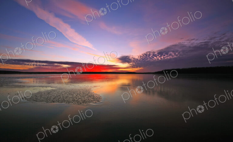 View of the sky and cloud patterns reflected in the frozen surface of a lake.