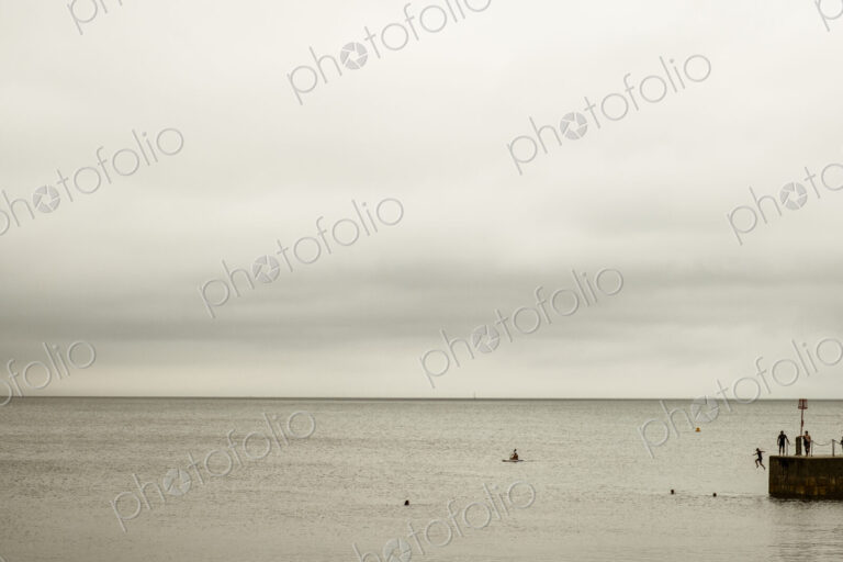 View out to sea, and people swimming and jumping off the harbour wall.