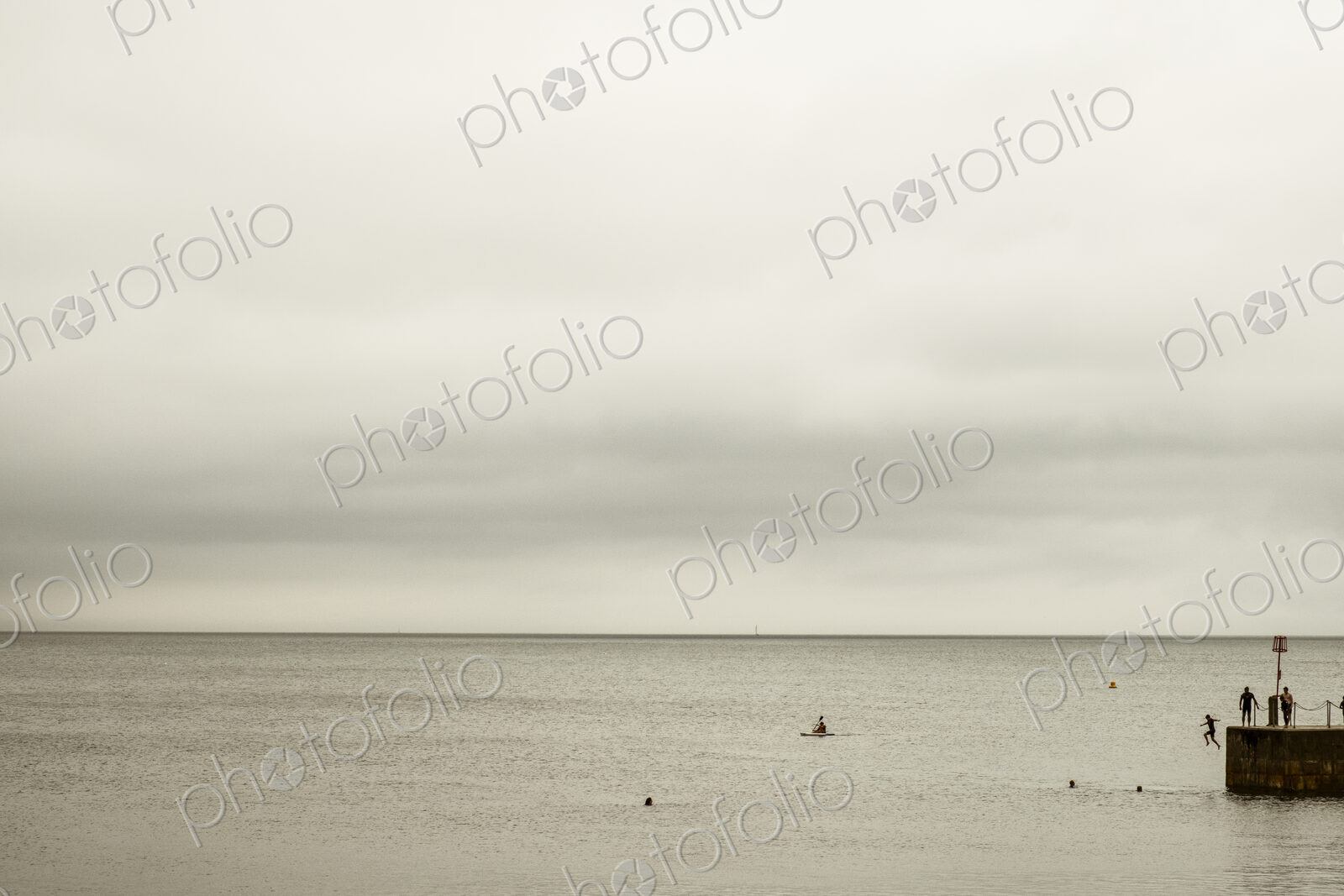 View out to sea, and people swimming and jumping off the harbour wall.