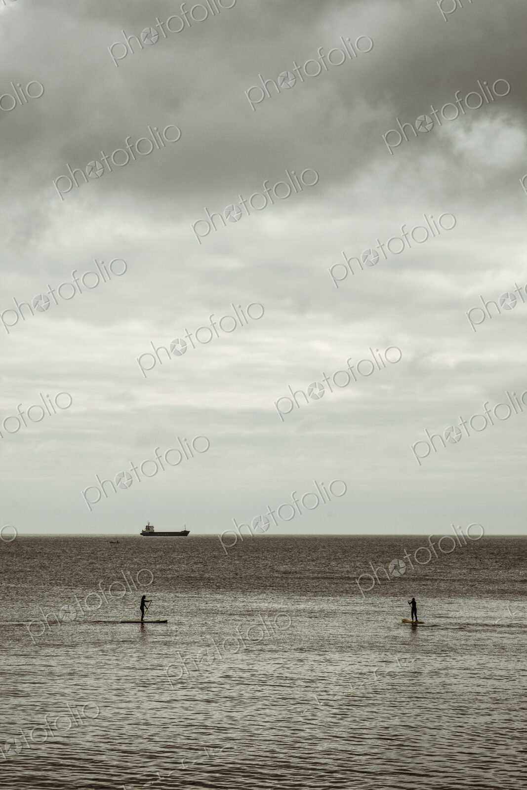View out to sea from the cliffs, two people paddleboarding on a calm sea, and a large…