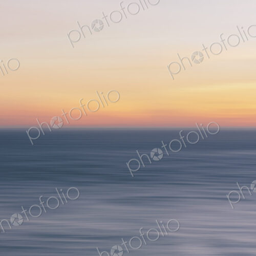 View out to sea over the ocean at dusk, a calm undulating sea surface.