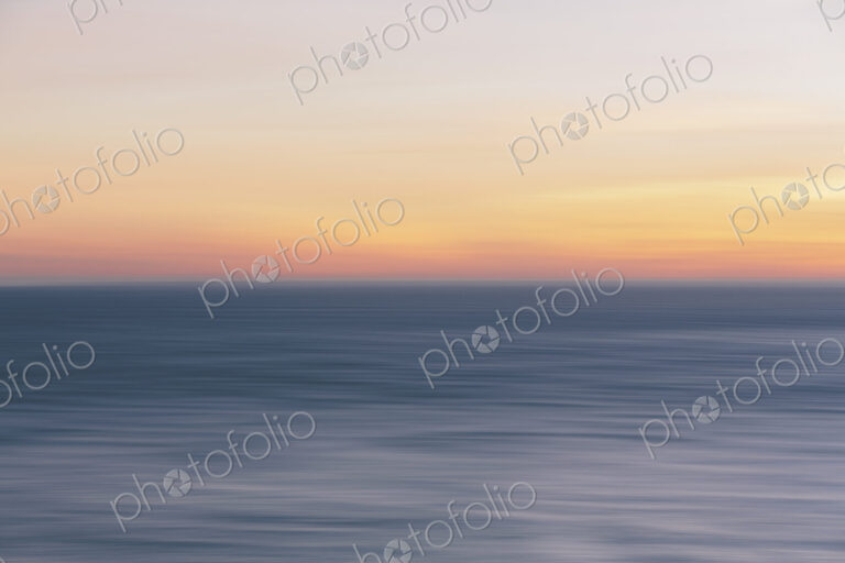 View out to sea over the ocean at dusk, a calm undulating sea surface.