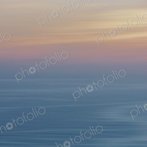 View out to sea over the ocean at dusk, the sunset light on the horizon and calm…