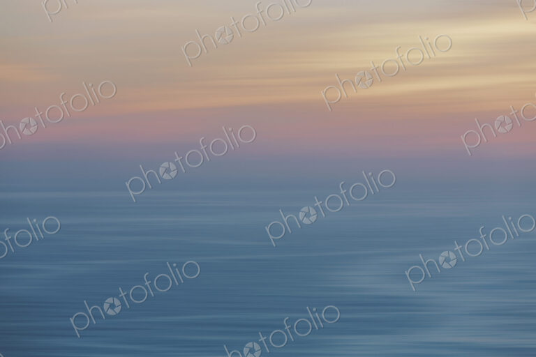View out to sea over the ocean at dusk, the sunset light on the horizon and calm…
