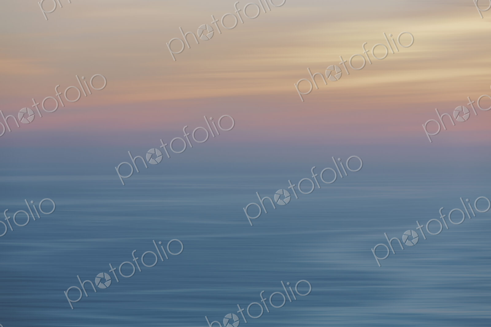 View out to sea over the ocean at dusk, the sunset light on the horizon and calm…