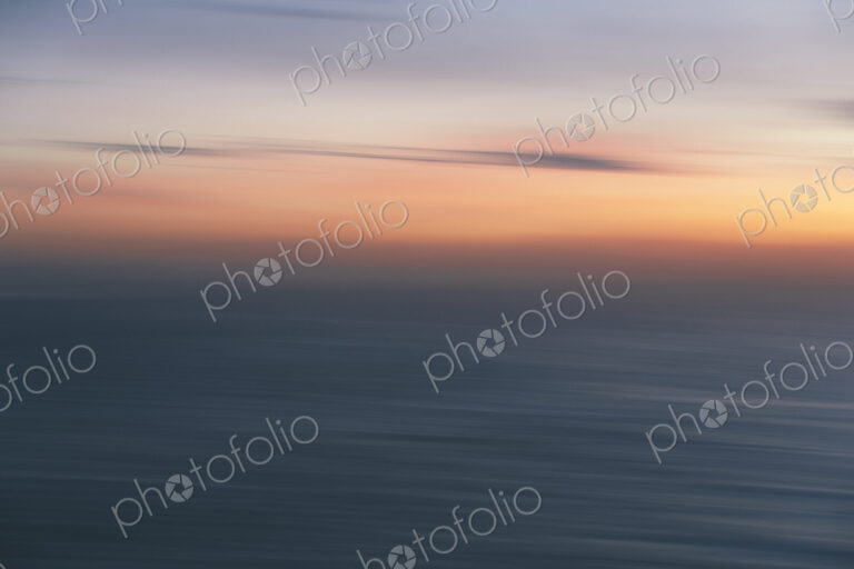 View out to sea over the ocean at dusk, the sunset light on the horizon and calm…