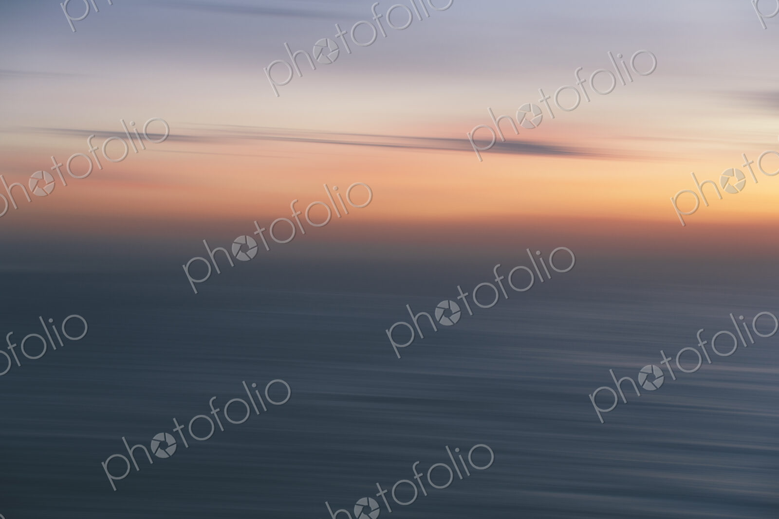 View out to sea over the ocean at dusk, the sunset light on the horizon and calm…