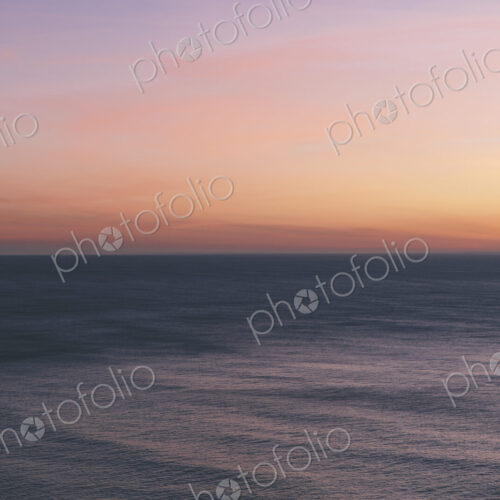 View out to sea over the ocean at dusk, the sunset light on the horizon and calm…