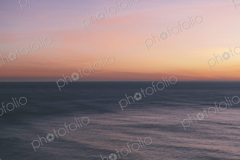 View out to sea over the ocean at dusk, the sunset light on the horizon and calm…