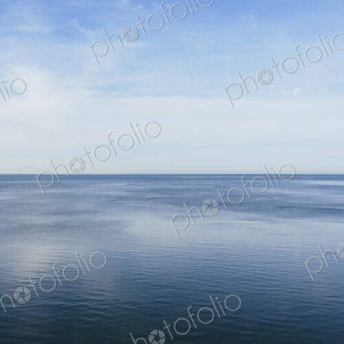 View out to the open sea from the coast. Flat calm water surface.