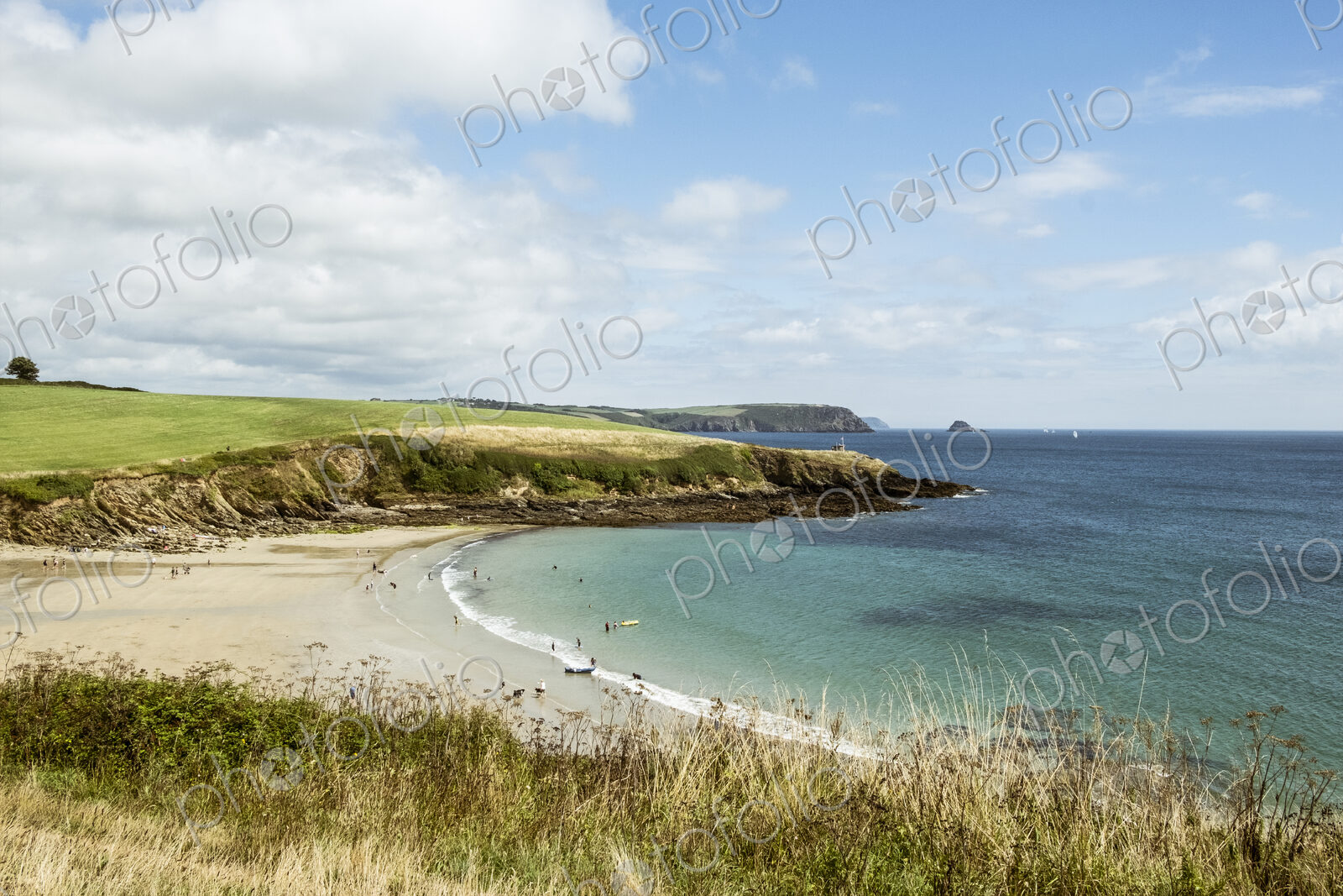 View over a sandy beach and cliffs in summer, a few people, clear shallow water and…
