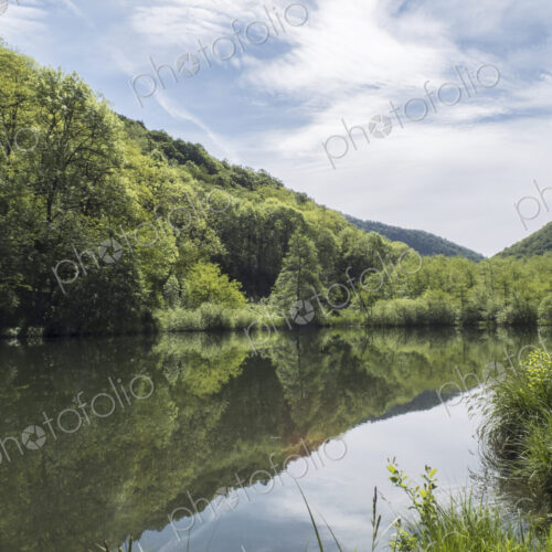 View over flat calm lake water, mountains and woodland, a boy on the shore.