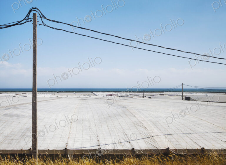 View over plastic greenhouses and crop cover, over a large area by the coast,…