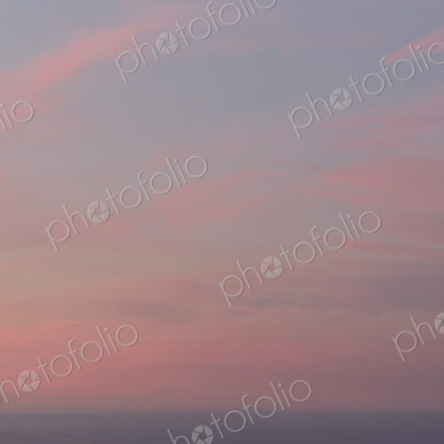 View over the ocean and the sunset sky with pink cloud at dusk.