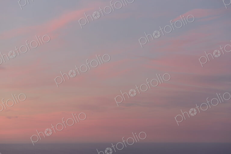 View over the ocean and the sunset sky with pink cloud at dusk.