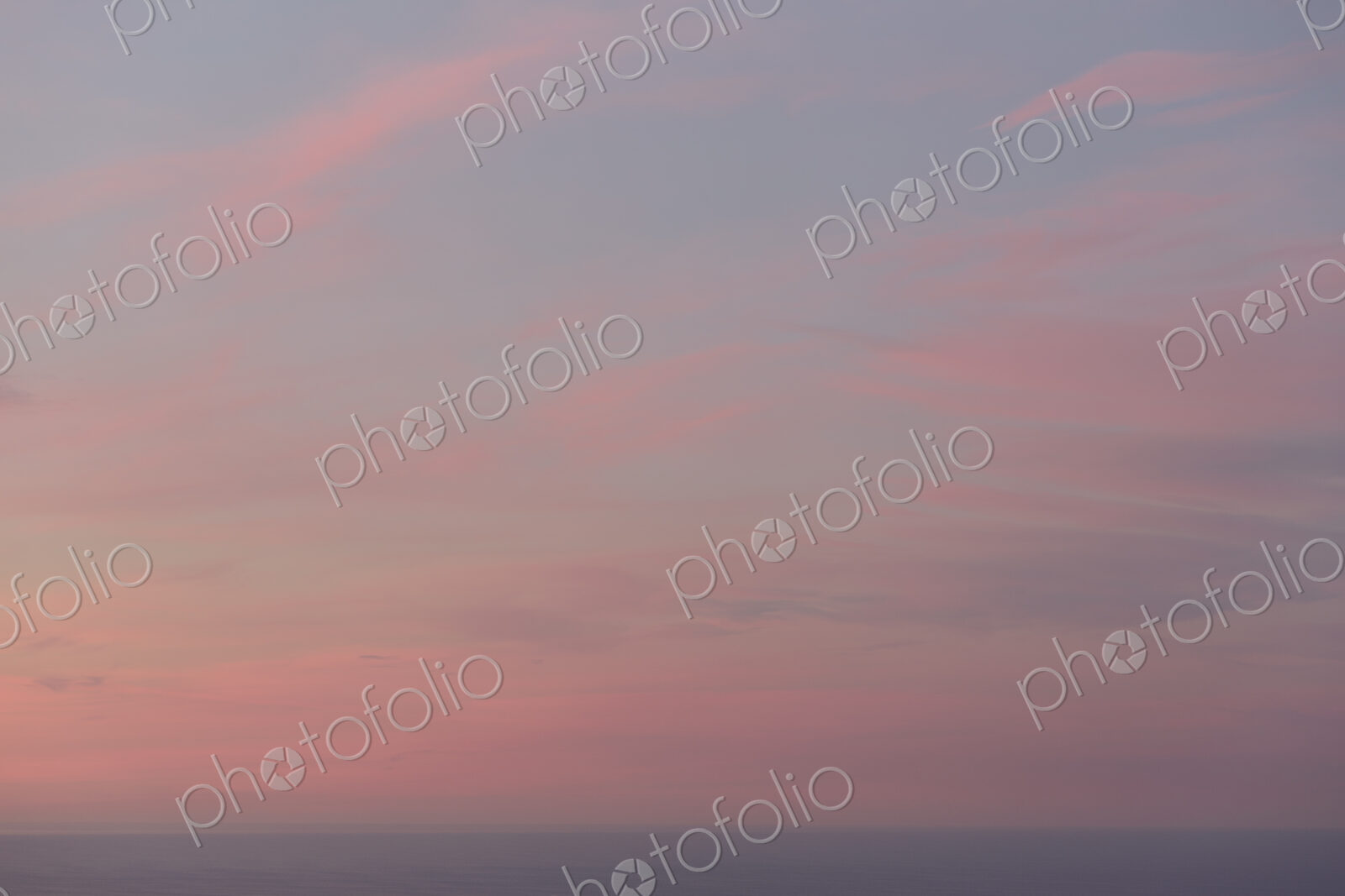 View over the ocean and the sunset sky with pink cloud at dusk.