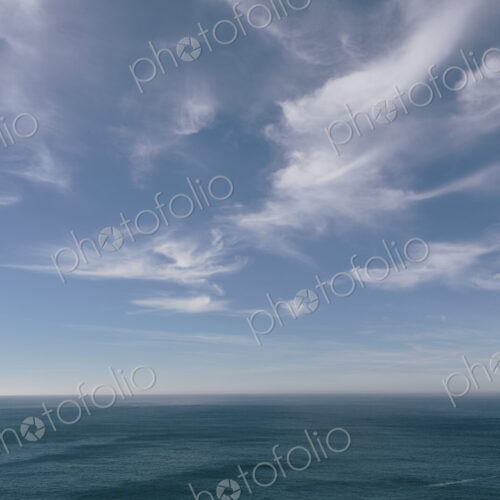 View over the ocean to the horizon, deep blue sea and light windblown wispy clouds in…
