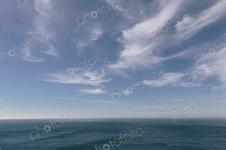 View over the ocean to the horizon, deep blue sea and light windblown wispy clouds in…