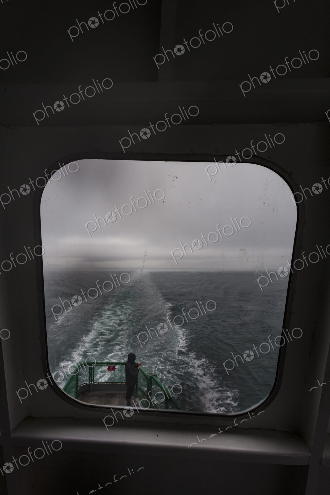 View through a ferry porthole window of the grey stormy weather in the San Juan…