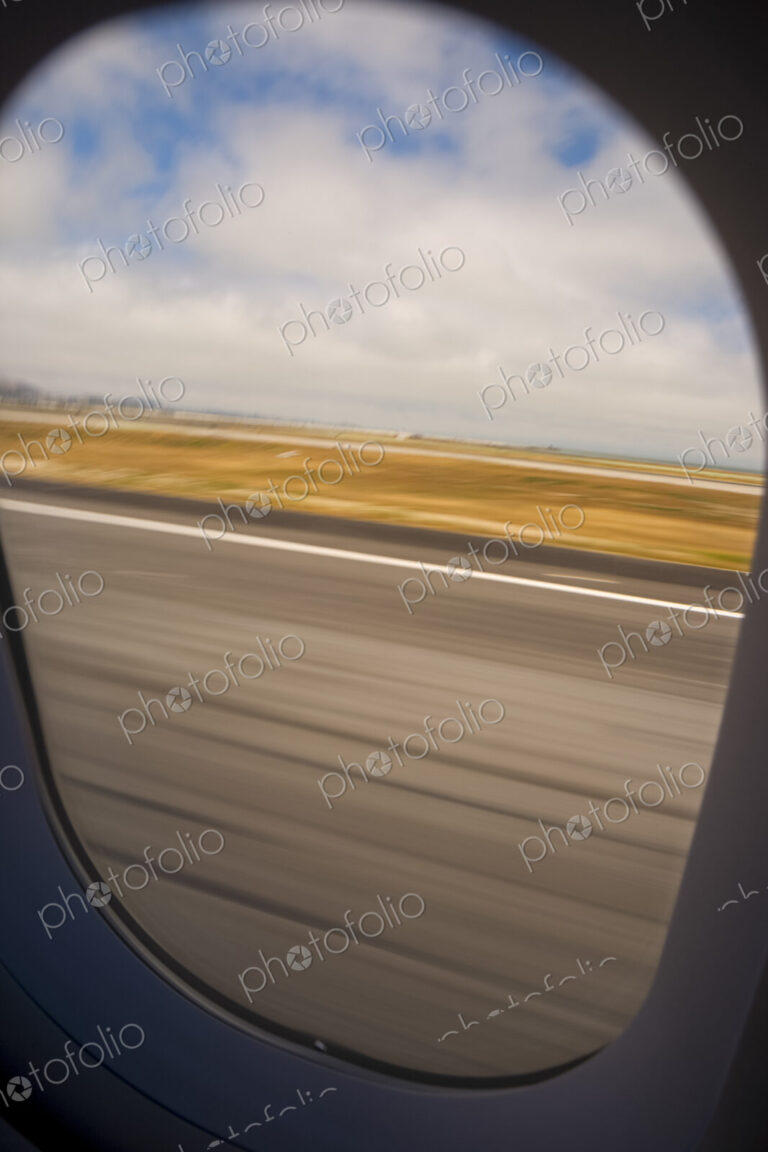View through an aircraft window of the runway during take off.