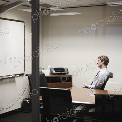 View through glass of a businessman working on a project in an office conference room. View through glass of a businessman working on a project in an office conference room.