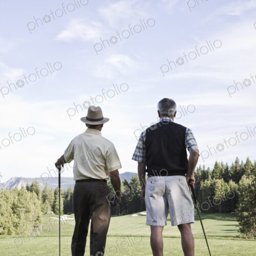 Viewed from behind, a pair of senior golfers check out a fairway on the golf course. Viewed from behind, a pair of senior golfers check out a fairway on the golf course.