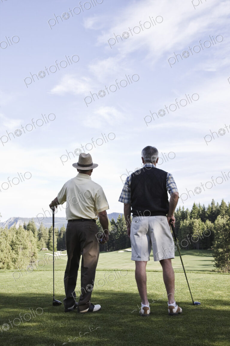 Viewed from behind, a pair of senior golfers check out a fairway on the golf course.