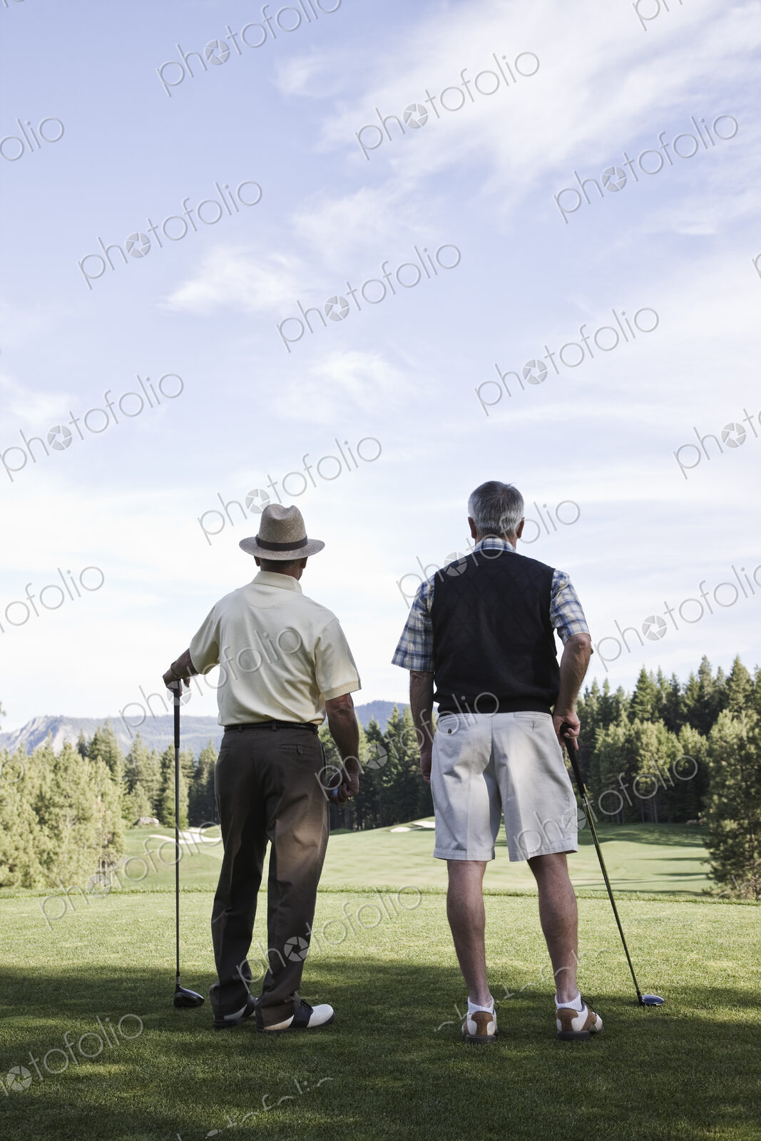 Viewed from behind, a pair of senior golfers check out a fairway on the golf course.