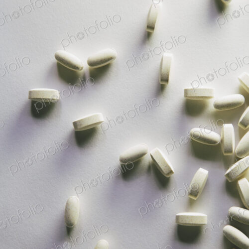 Vitamin C supplements, white oval tablets spread on a white background.