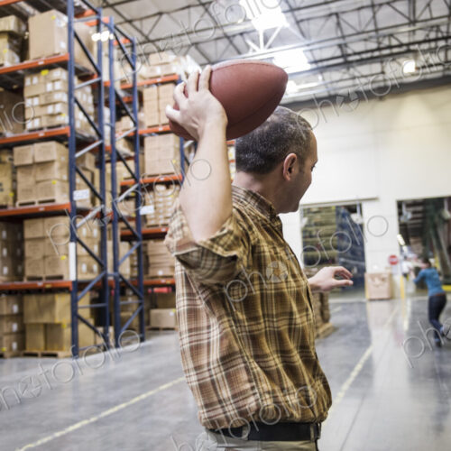 Warehouse employees playing catch with an American football during a work break in a… Warehouse employees playing catch with an American football during a work break in a…