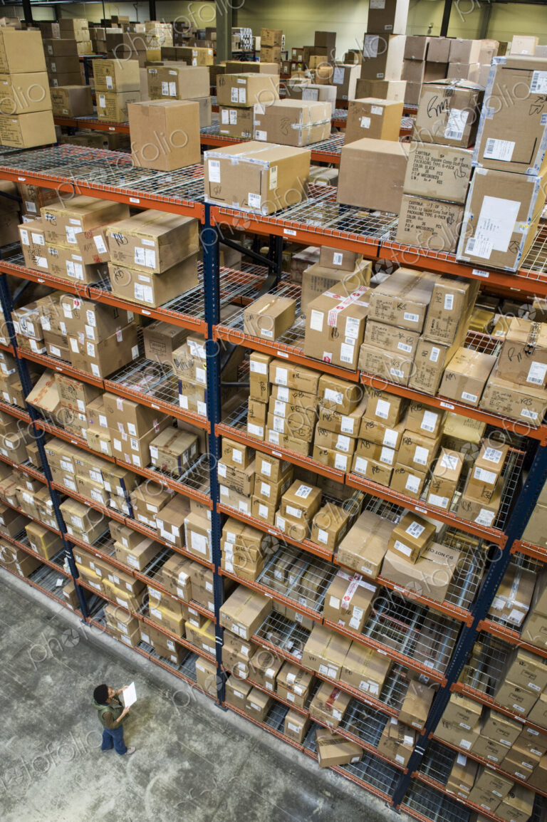 Warehouse worker checking inventory of boxes on racks in a distribution warehouse.