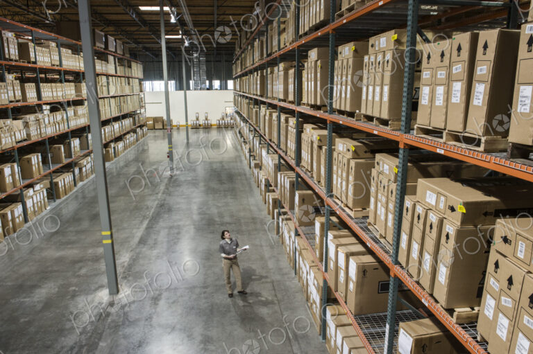 Warehouse worker checking inventory of stock on racks in a distribution warehouse.