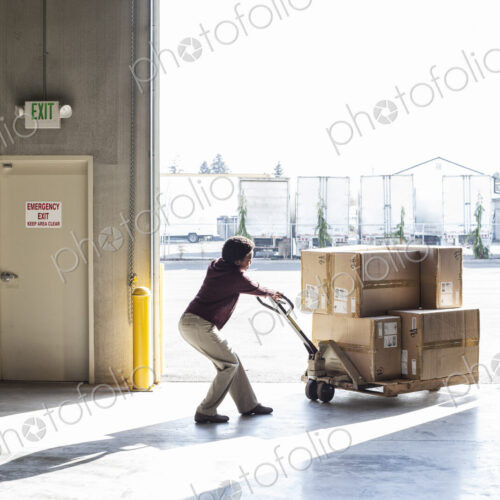 Warehouse worker moving products in cardboard boxes using a manual pallet jack Warehouse worker moving products in cardboard boxes using a manual pallet jack
