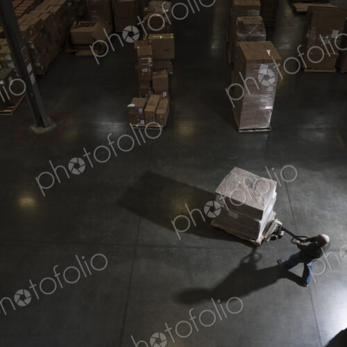 Warehouse worker using a manual pallet jack to move some products in a distribution…