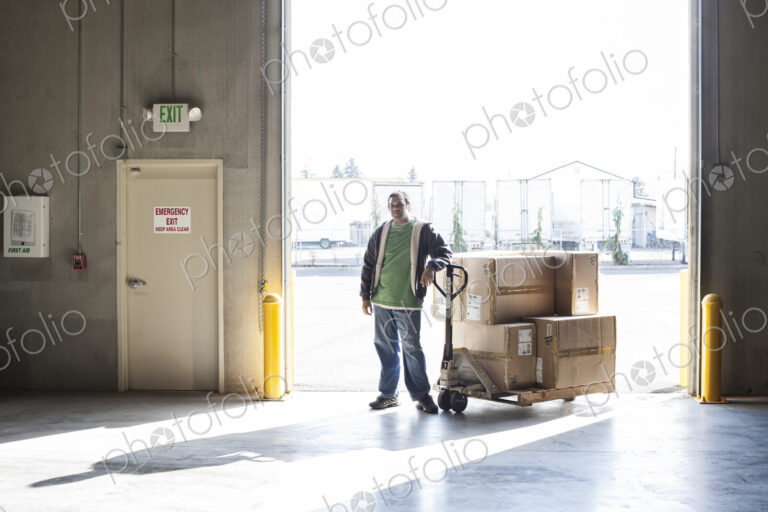 Warehouse worker with manual pallet jack and cardboard boxes in a distribution warehouse.