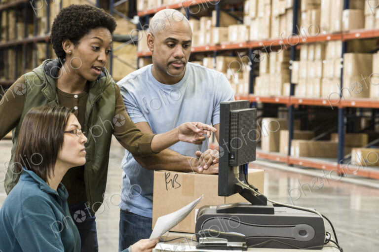 Warehouse workers checking inventory on a computer in a large distrubiton warehouse.