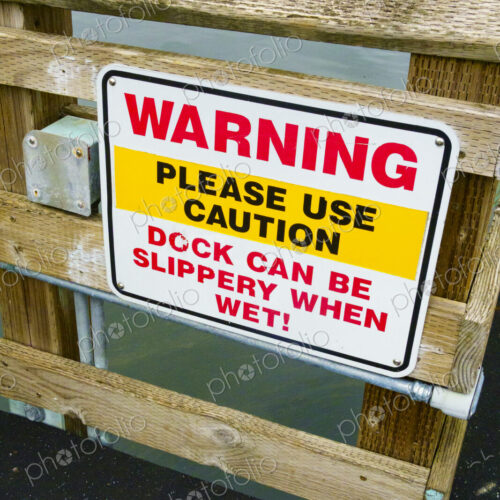 Warning sign on a wooden dock, red lettering, Please Use Caution, Deck can be slippery… Warning sign on a wooden dock, red lettering, Please Use Caution, Deck can be slippery…