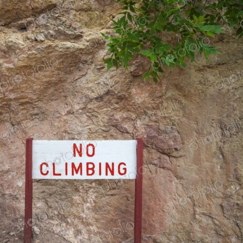 Warning sign reading "No Climbing" in red letters, mounted on wooden posts, placed…