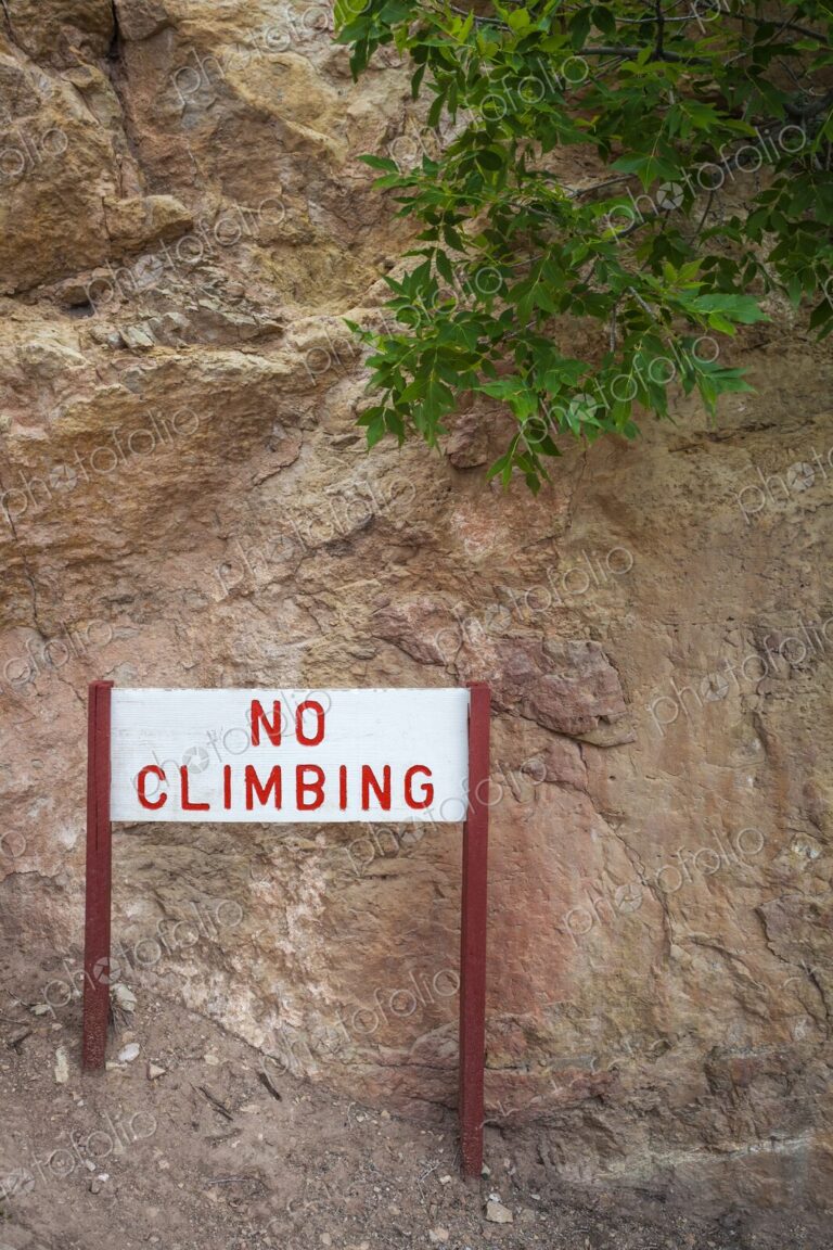Warning sign reading "No Climbing" in red letters, mounted on wooden posts, placed…