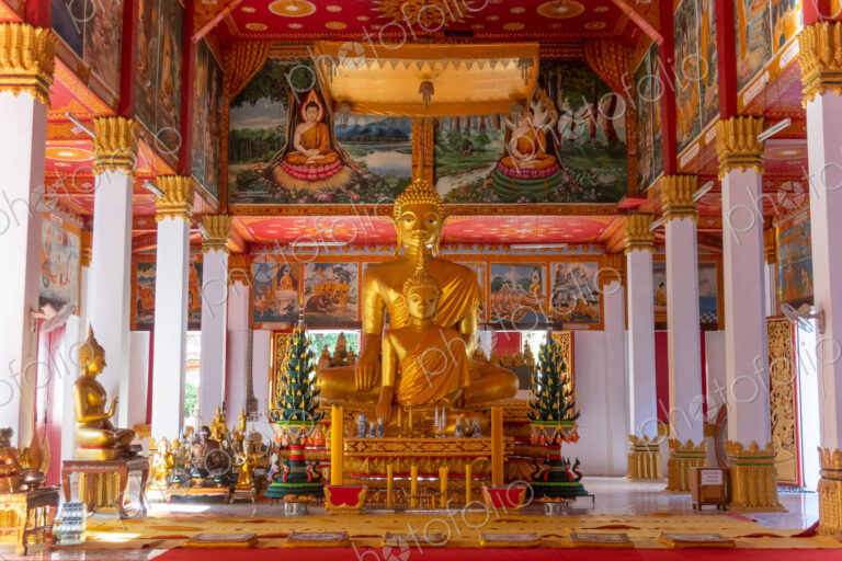 Wat Si Saket, a large golden Buddha statue and altar with offerings and wall murals,…