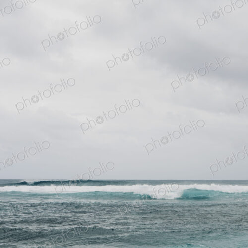 Waves breaking on a beach, turquoise water and an overcast sky.