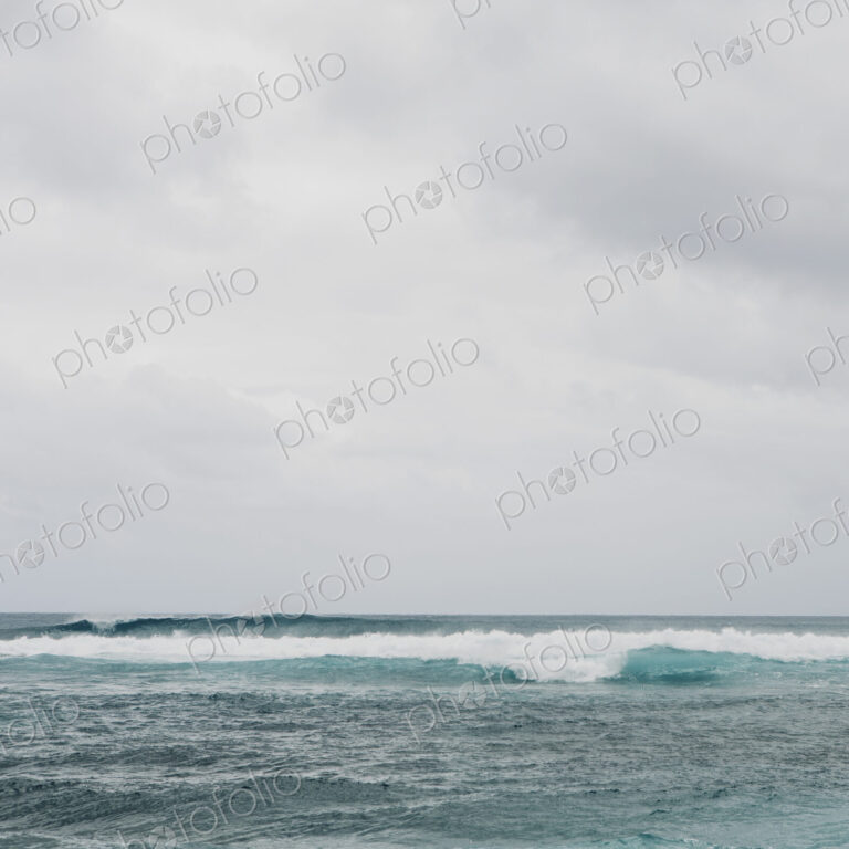 Waves breaking on a beach, turquoise water and an overcast sky.