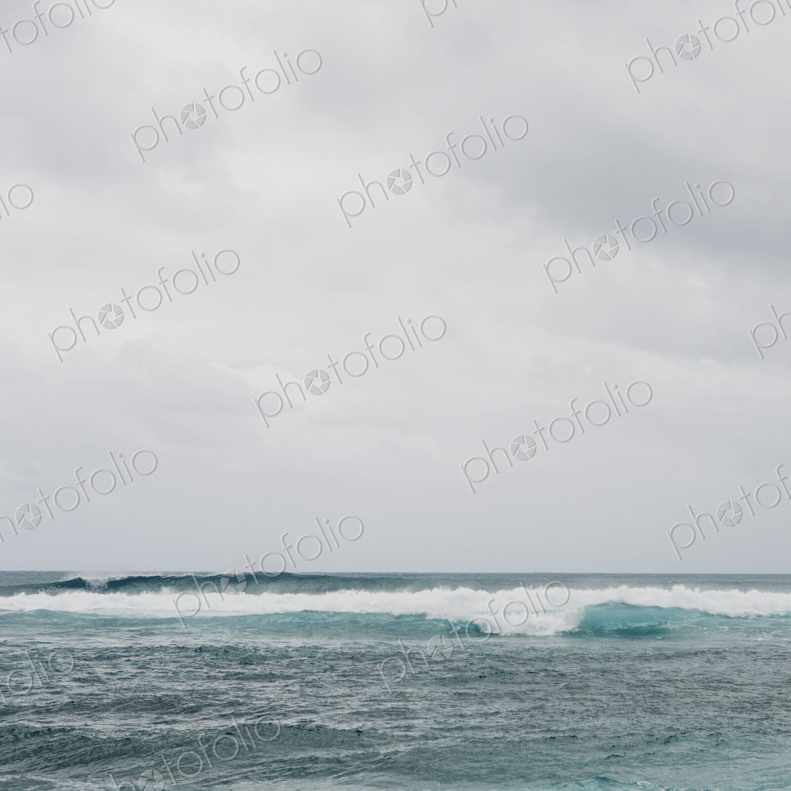 Waves breaking on a beach, turquoise water and an overcast sky.