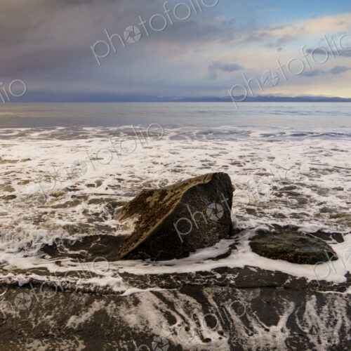 Waves surrounding boulder on beach along the Strait of Juan de Fuca, Port Angeles, WA USA Waves surrounding boulder on beach along the Strait of Juan de Fuca, Port Angeles, WA USA
